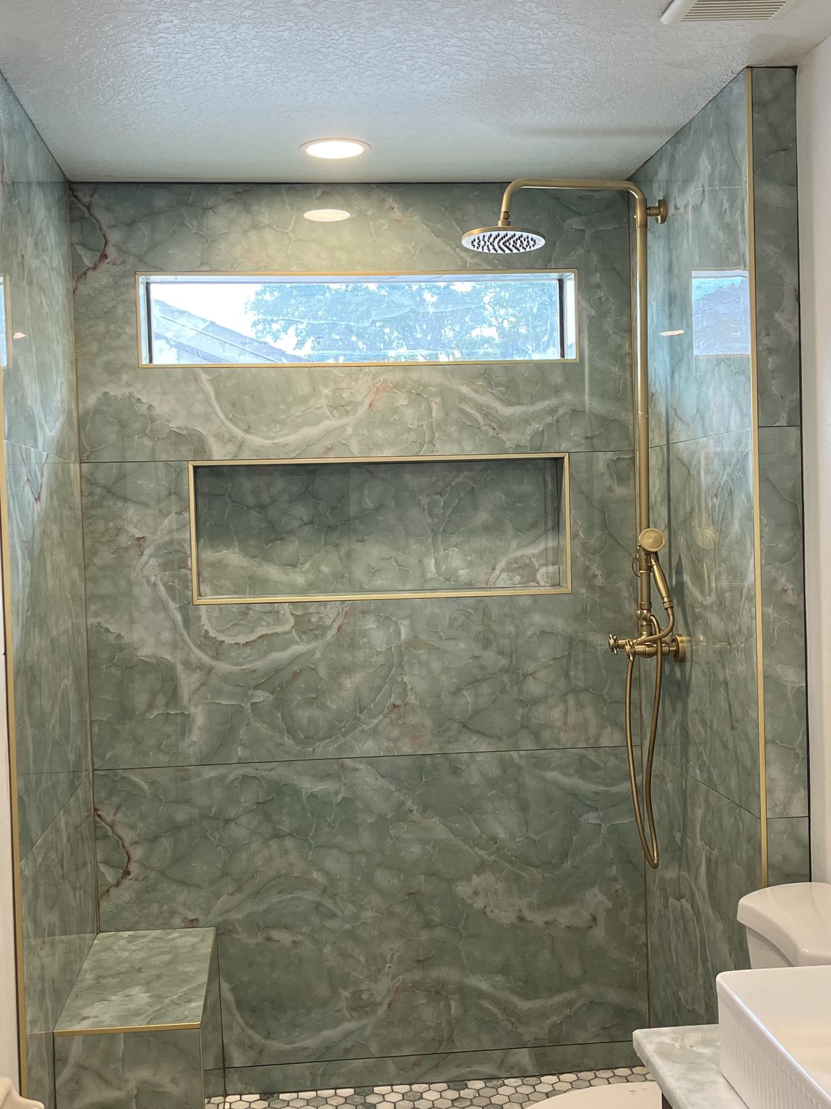 Custom shower with sage-green marble tile and brass fixtures